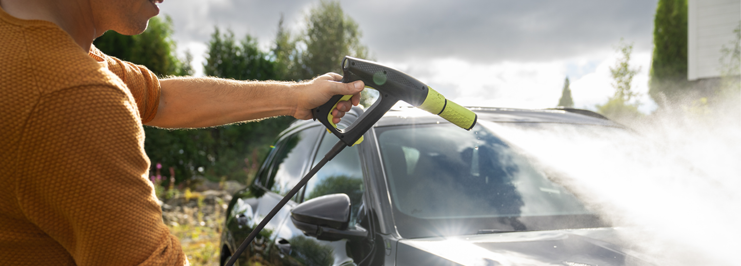 Person using a high-pressure washer to clean a car outdoors.